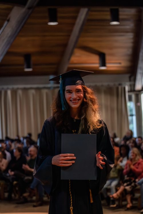 Student smiling in graduation gown holding certificate
